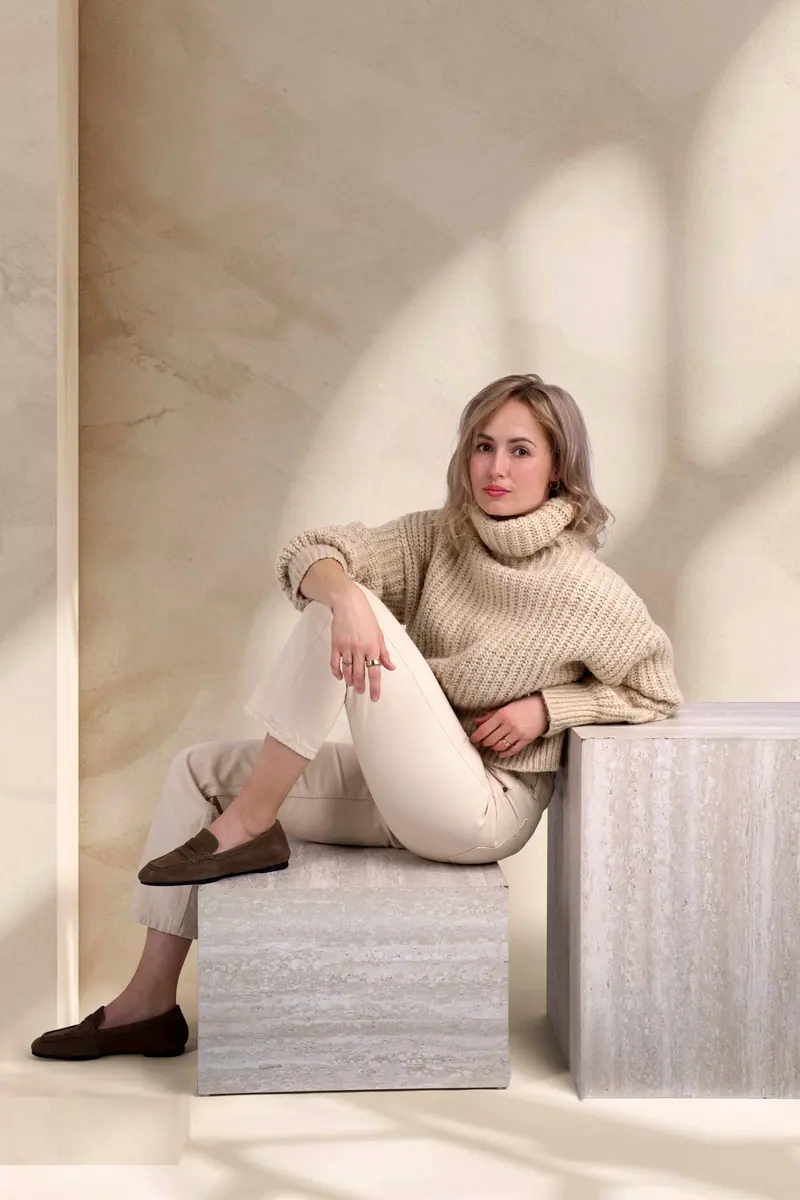 Lifestyle fotenie — žena v béžovom svetri sedí na travertínovom podstavci