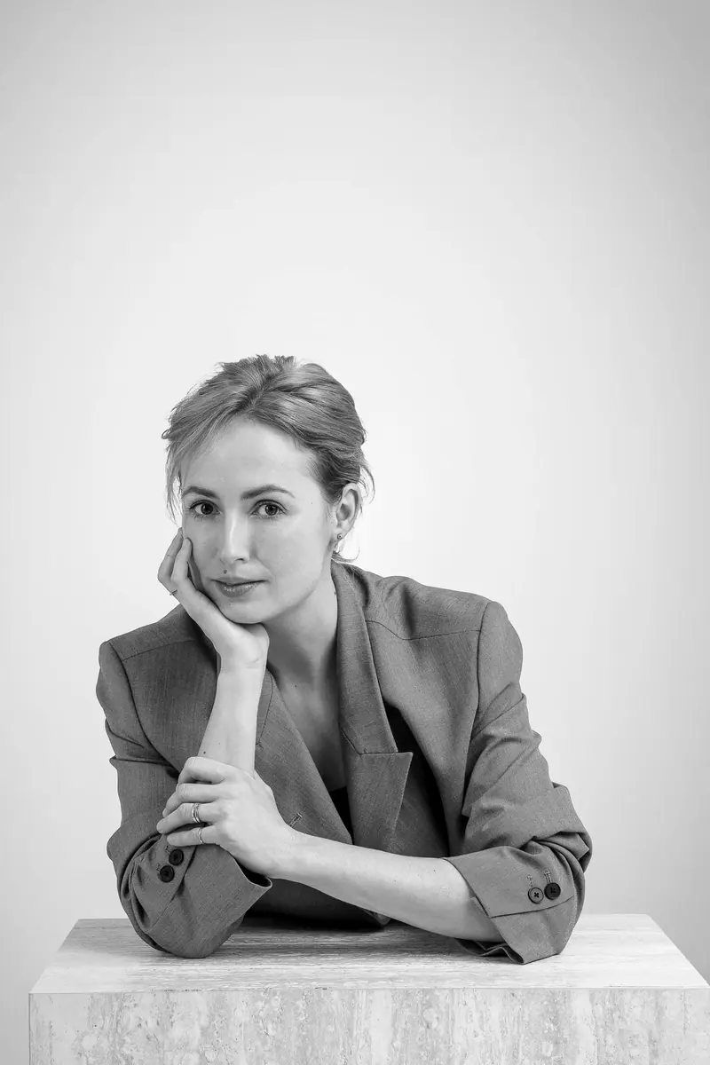 Lifestyle fotenie — žena v saku sa opiera o kamenný podstavec, dlaň pri tvári — čiernobiela