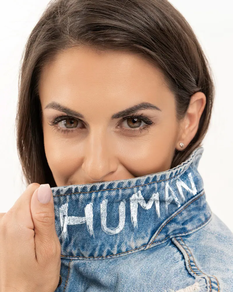 Lifestyle fotenie — žena si zakrýva ústa golierom džínsovej bundy s nápisom HUMAN