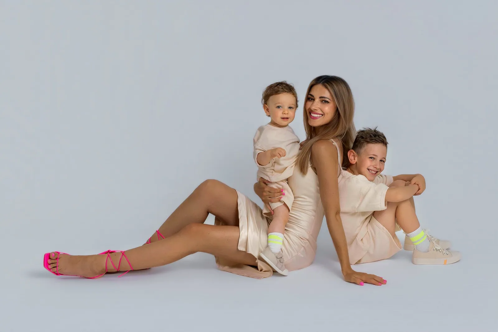 Mama a deti — mama sedí na zemi opretá o staršieho syna a drží malého synčeka; na mobile dievčatko objíma plyšového tučniaka