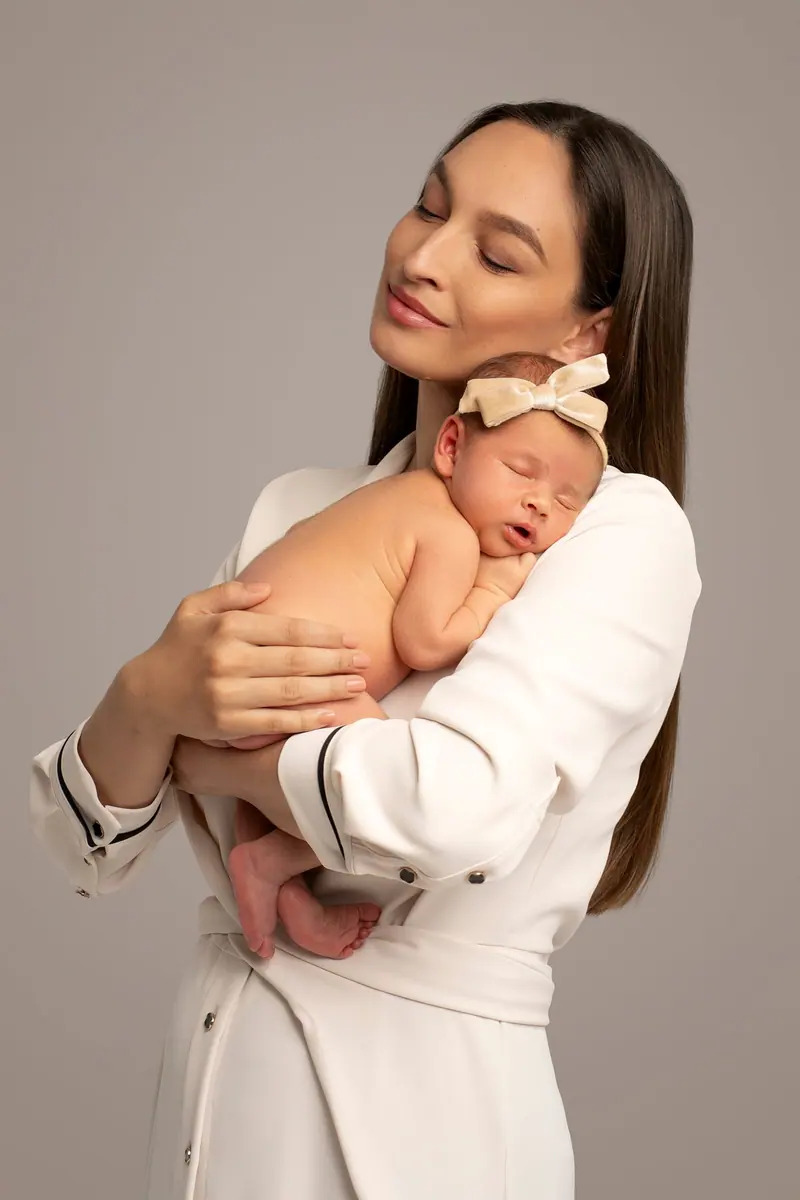 Fotenie mama a baby — mama v krémovom kabáte drží novorodenca, sivé pozadie