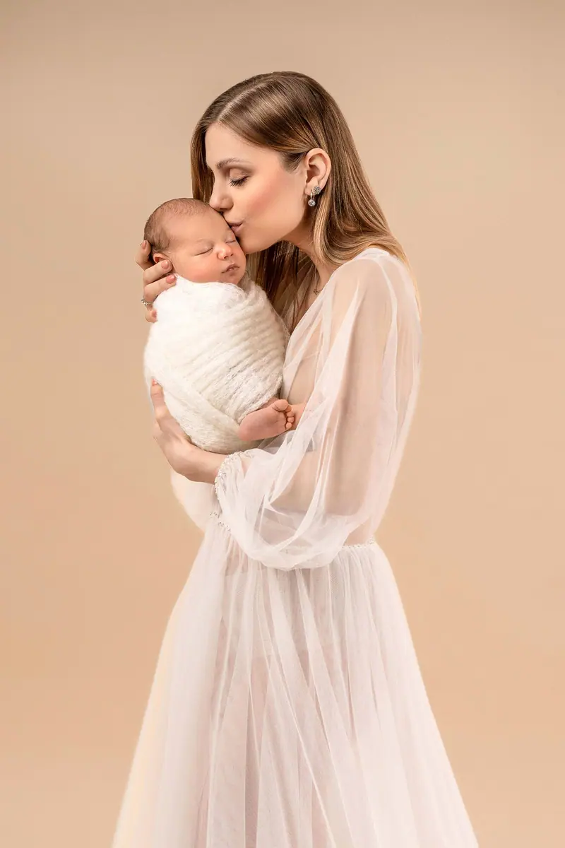 Fotenie mama a baby — mama v tylových šatách bozkáva zavinuté bábätko