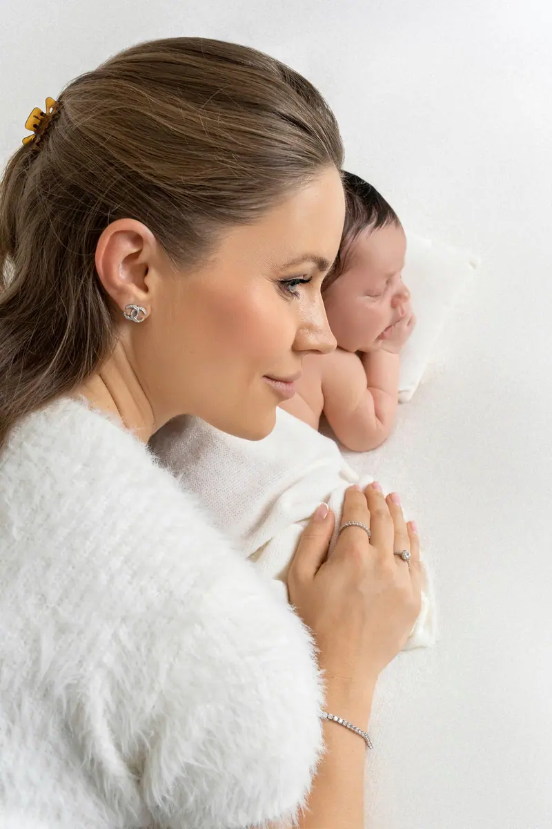 Fotenie mama a baby — mama v bielom svetri s novorodencom na ramene, profil