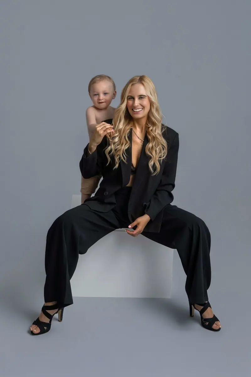 Fotenie mama a baby — blond mama v čiernom obleku sedí na kocke s bábätkom
