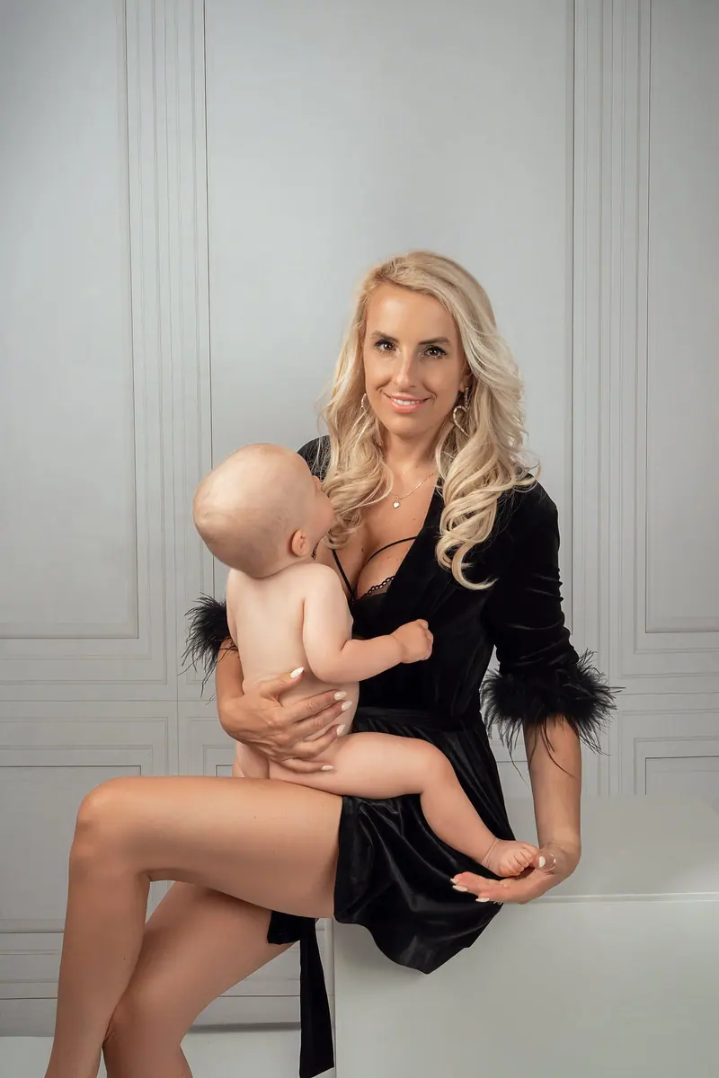 Fotenie mama a baby — blond mama v čiernom drží bábätko, biely panelový interiér