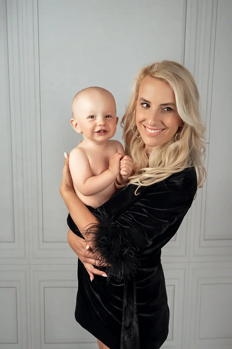 Fotenie mama a baby — blond mama v čiernom s bábätkom na ramene, biely panel