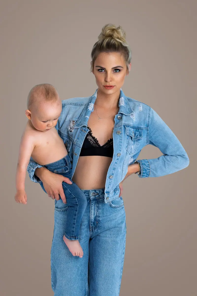 Fotenie mama a baby — mama v džínsovej bunde drží bábätko na boku