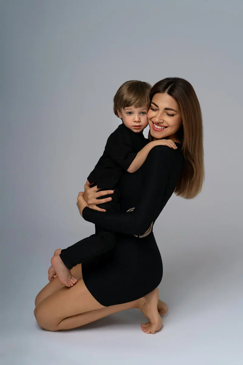 Fotenie mama a baby — mama v čiernom drží syna, sivé pozadie