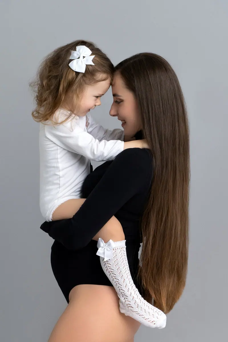 Fotenie mama a baby — mama v čiernom drží dcérku s mašľou, čelo pri čele
