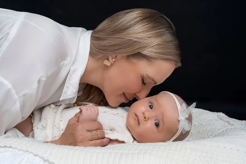 Fotenie mama a baby — mama v bielej košeli leží pri bábätku s čelenkou, čierne pozadie