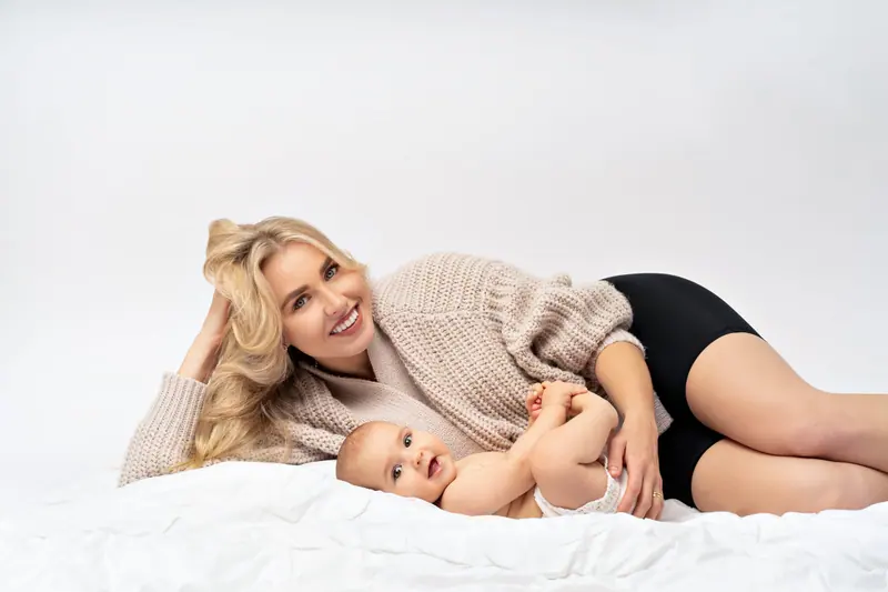 Fotenie mama a baby — mama v pletenom svetri leží pri bábätku na bielej deke