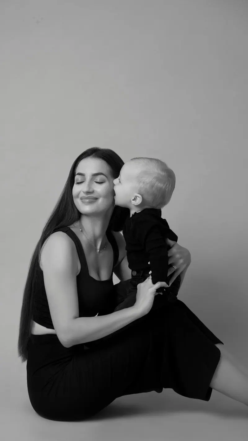 Fotenie mama a baby — mama v čiernom, bábätko ju bozkáva na líce — čiernobiela