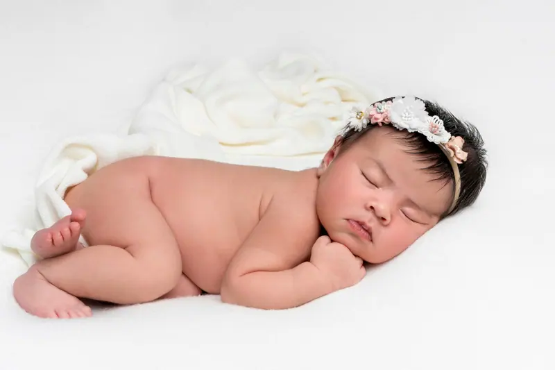 Newborn fotenie — novorodenec s kvetinovou čelenkou spí na bruchu