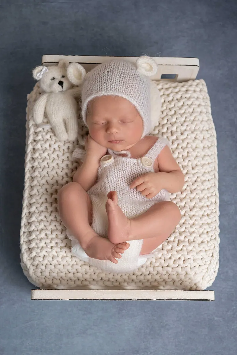 Newborn fotenie — novorodenec v pletenej postieľke s čiapkou, modré pozadie