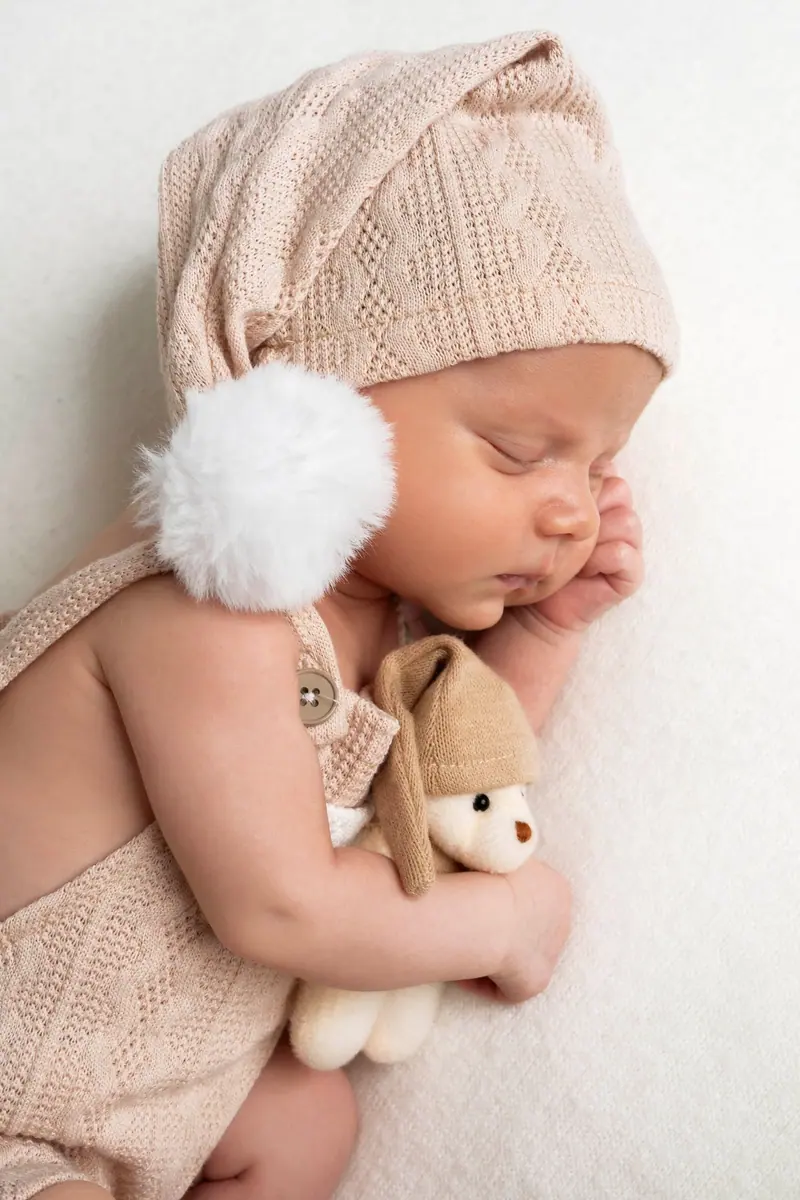 Newborn fotenie — novorodenec v ružovej čiapke s brmbolcom drží plyšovú hračku
