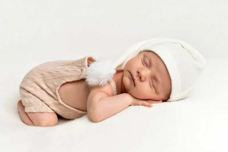 Newborn fotenie — novorodenec spí na bruchu v čiapke