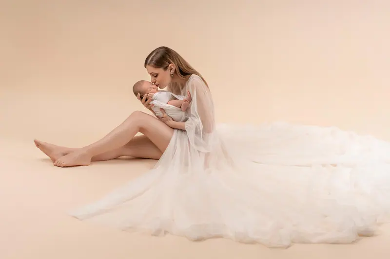 Fotenie mama a baby — mama v tylových šatách sedí s novorodencom, široký záber