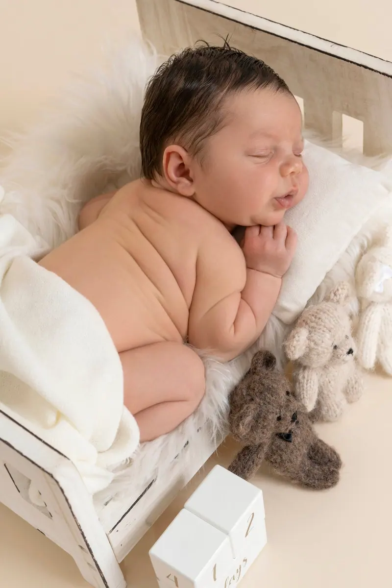 Newborn fotenie — novorodenec spí v drevenej postieľke s plyšovou hračkou