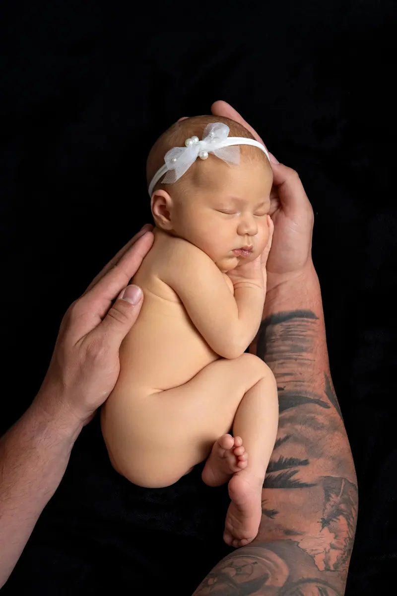 Newborn fotenie — novorodenec v tetovaných rukách otca, čierne pozadie