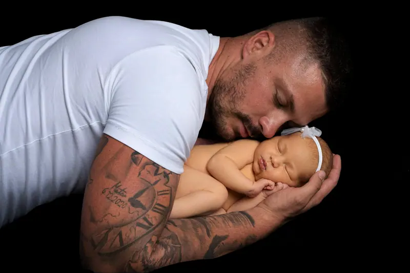 Newborn fotenie — otec sa skláňa nad novorodencom, čierne pozadie
