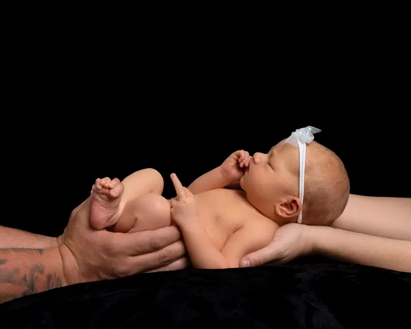 Newborn fotenie — novorodenec držaný v rukách, čierne pozadie