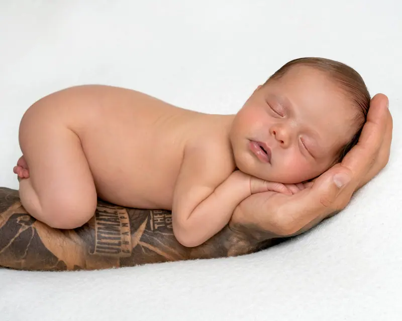 Newborn fotenie — novorodenec spí na tetovanom predlaktí otca