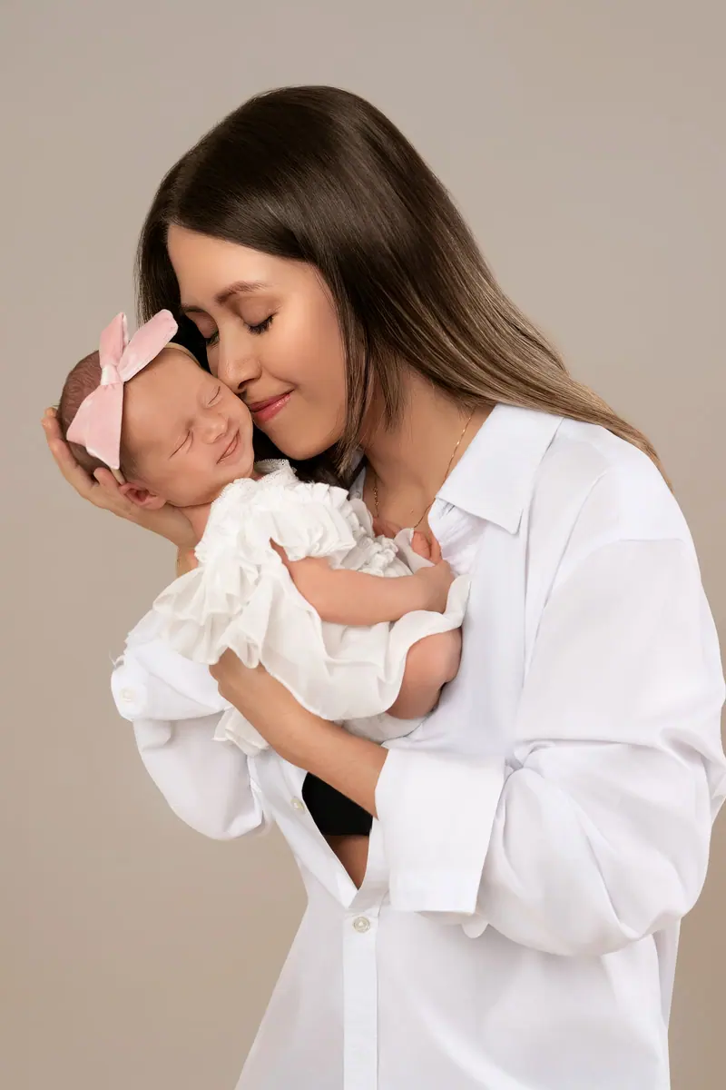 Newborn fotenie — mama v bielej košeli s novorodencom pri tvári, béžové pozadie