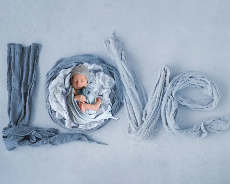 Newborn fotenie — nápis „LOVE“ z modrých šatiek, novorodenec v písmene O, zhora