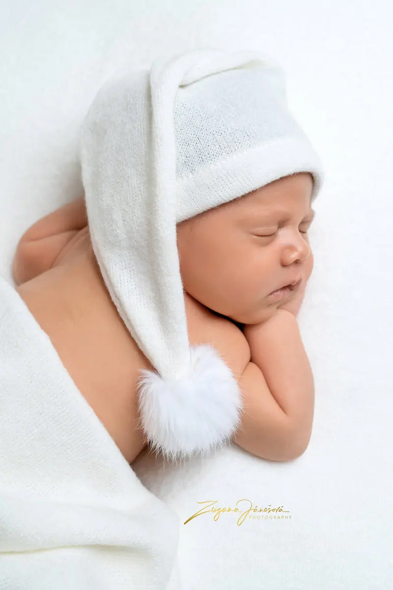 Newborn fotenie — spiace bábätko v bielej čiapke so strapcom