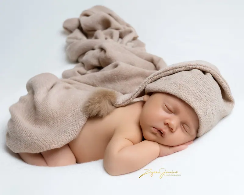 Newborn fotenie — spiace bábätko na béžovej deke v čiapke so strapcom
