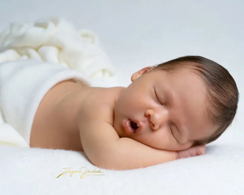 Newborn fotenie — spiace bábätko na bruchu na bielej deke