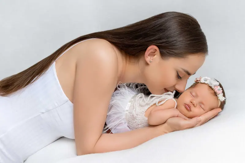 Newborn fotenie — mama v bielom leží pri novorodencovi s čelenkou