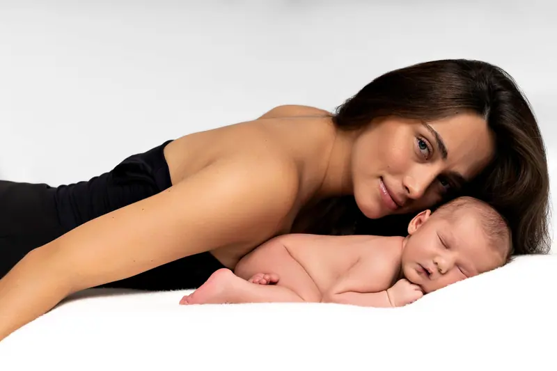 Newborn fotenie — mama leží za novorodencom, obaja na bielej deke