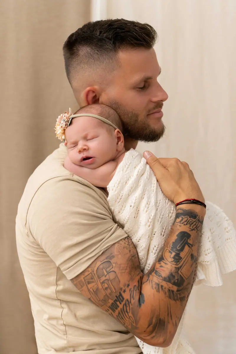 Newborn fotenie — tetovaný otec drží novorodenca na pleci