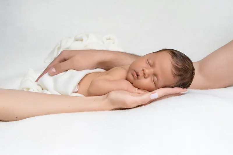 Newborn fotenie — novorodenec na rukách mamy, bielo-krémová