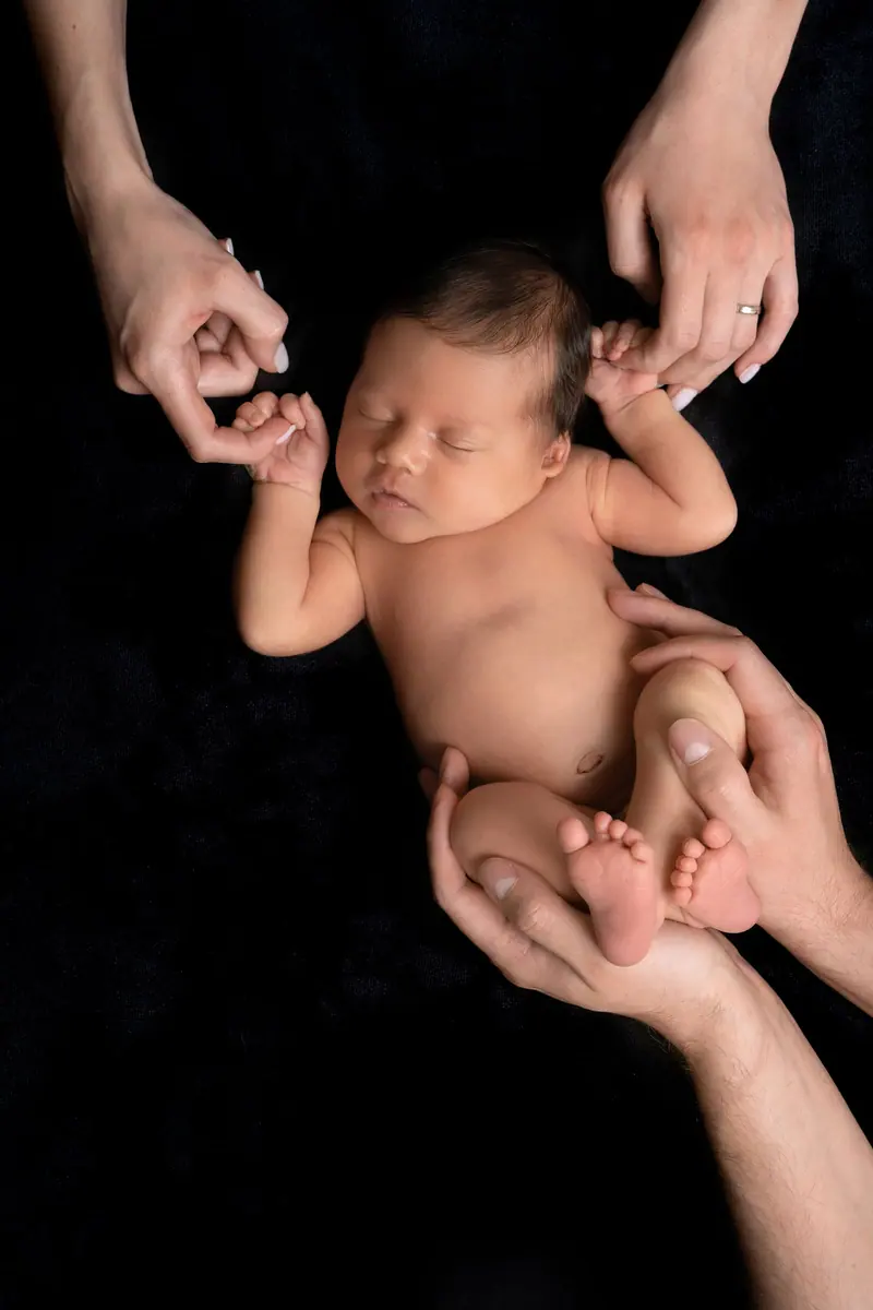 Newborn fotenie — novorodenec v rukách rodičov, čierne pozadie