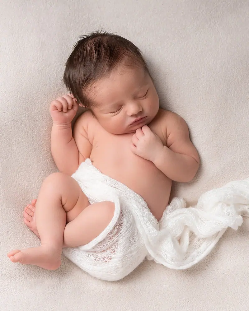 Newborn fotenie — spiaci novorodenec na krémovej deke, záber zhora