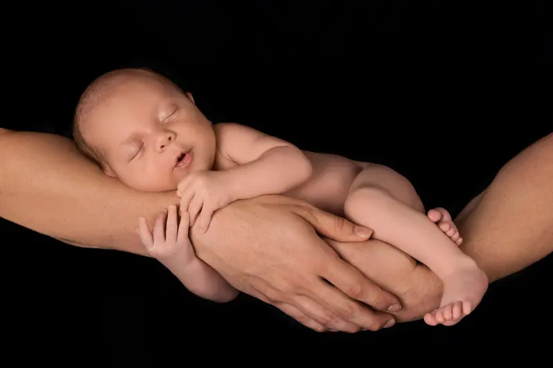 Newborn fotenie — novorodenec v rukách otca, čierne pozadie