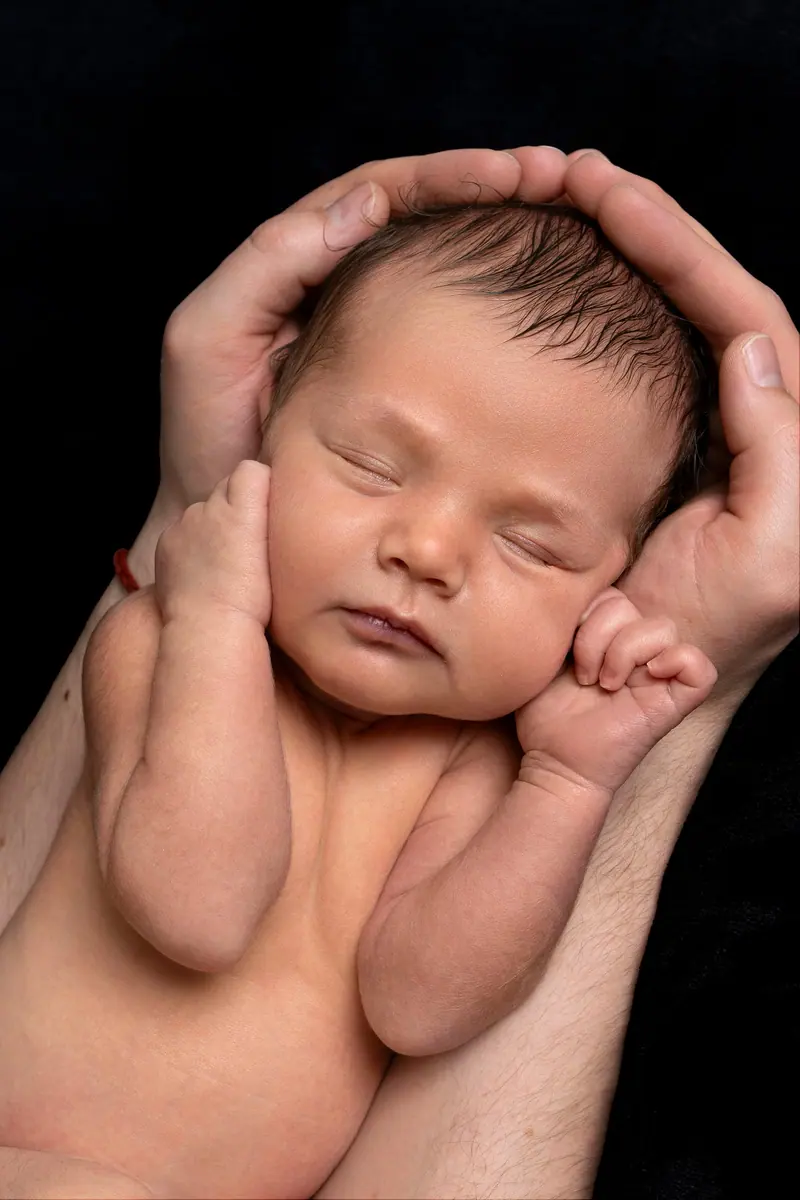 Newborn fotenie — hlavička novorodenca v dlaniach, čierne pozadie