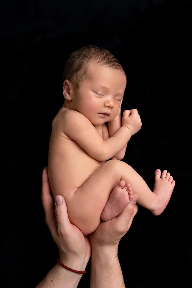 Newborn fotenie — schúlený novorodenec v dlaniach, čierne pozadie