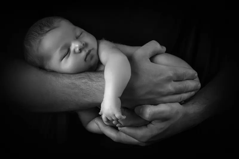 Newborn fotenie — novorodenec v rukách otca, čierne pozadie — čiernobiela