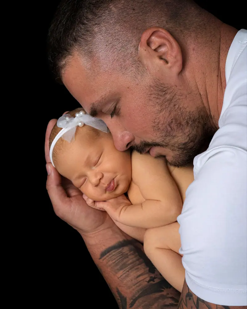 Newborn fotenie — otec s tvárou pri novorodencovi s mašľou, čierne pozadie