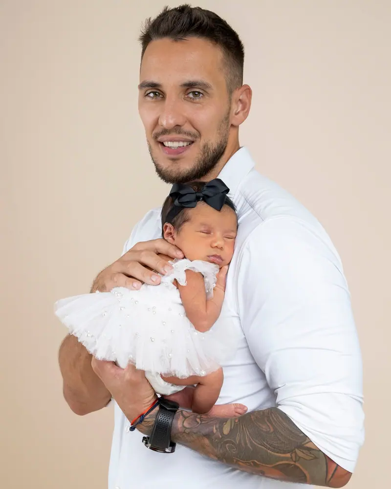 Newborn fotenie — otec v bielom drží novorodenca v tutu sukienke