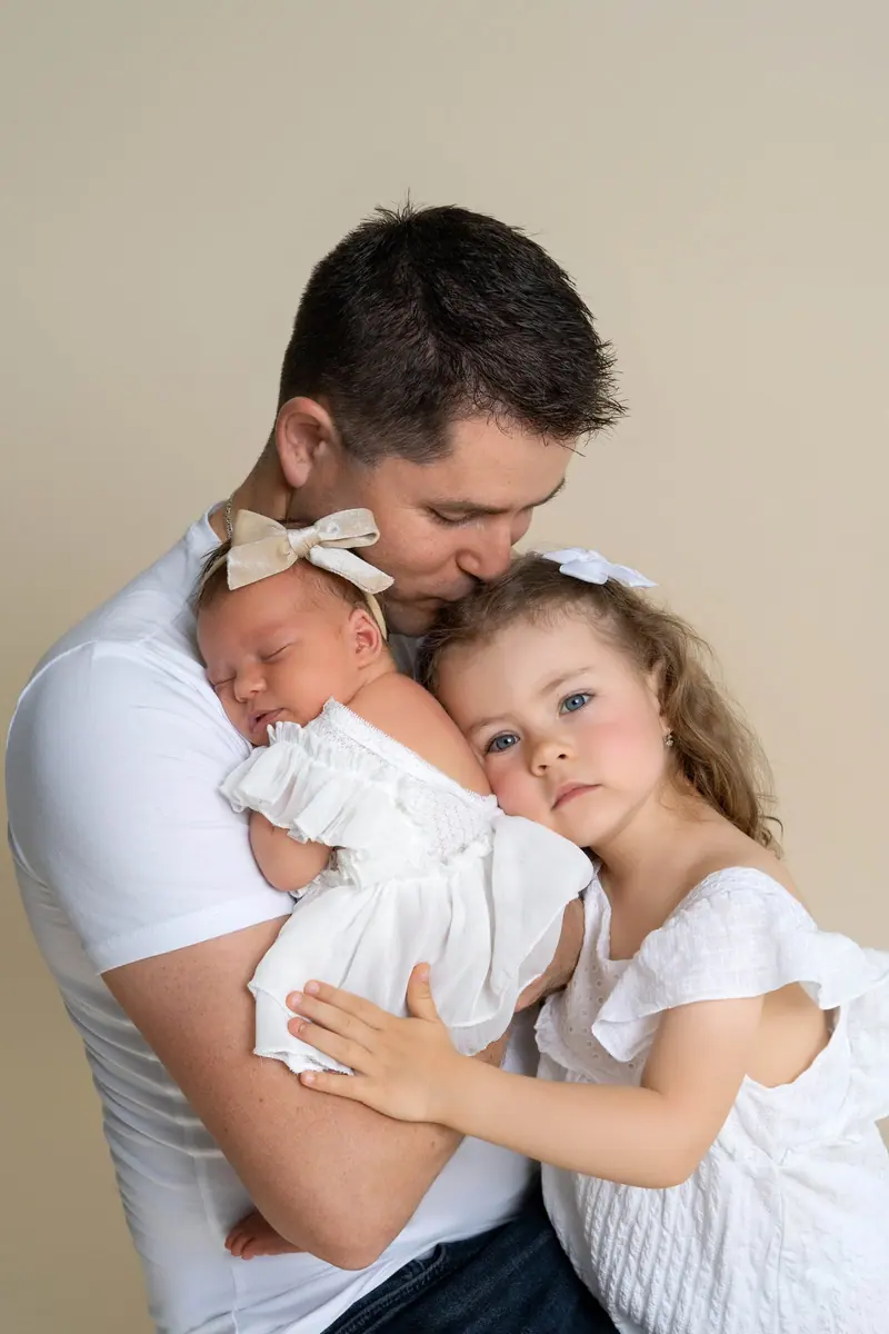 Newborn fotenie — otec drží novorodenca, staršia sestra sa túli