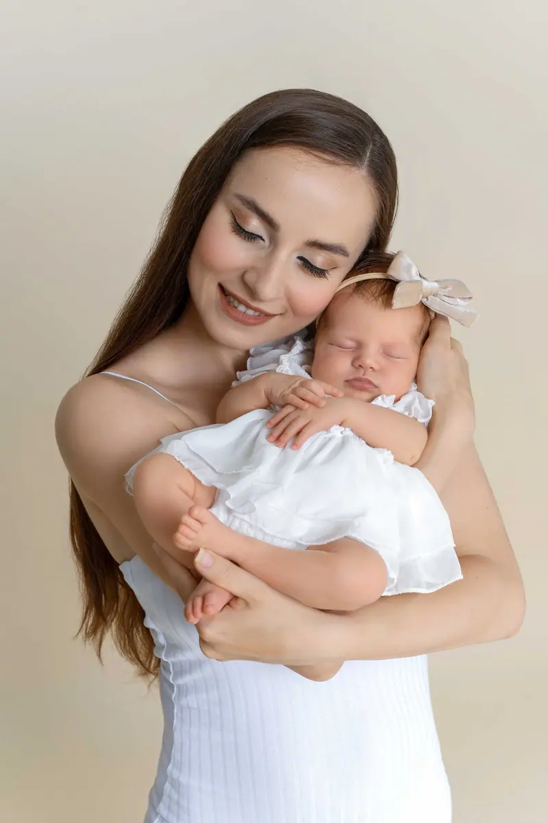 Newborn fotenie — mama v bielom drží novorodenca