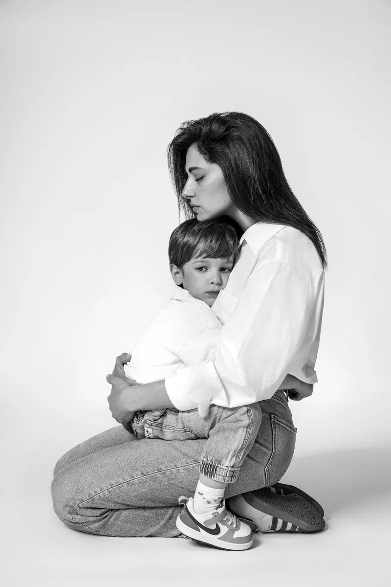 Rodinné fotenie — mama kľačí a objíma syna — čiernobiela