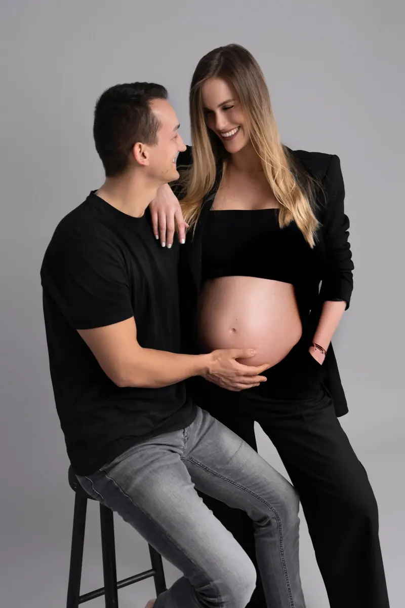 Tehotenské fotenie — pár na stoličke, muž drží bruško