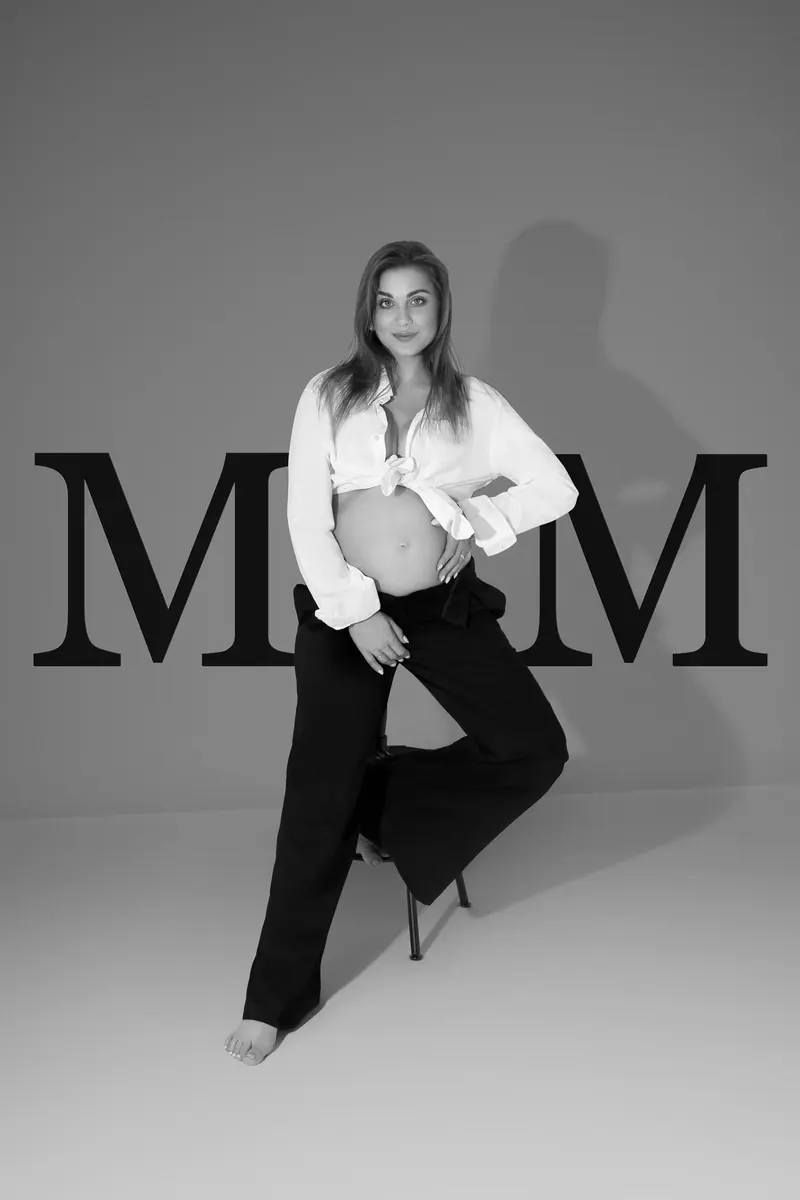 Tehotenské fotenie — tehotná v bielej košeli pred nápisom „MOM“ — čiernobiela