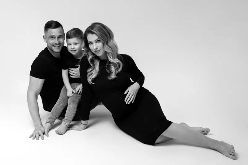 Tehotenské fotenie — rodina so synom sedí na zemi, tehotná v čiernych šatách — čiernobiela