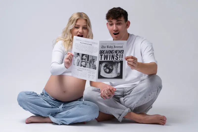 Tehotenské fotenie — pár sedí na zemi s novinami „Breaking news: TWINS“